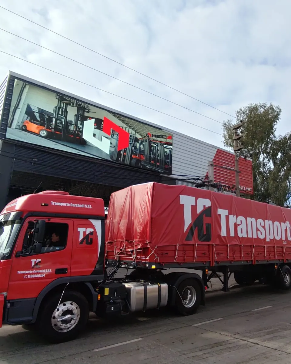 Camión con semirremolque de Transporte Carchedi con lona roja, estacionado frente a un depósito
